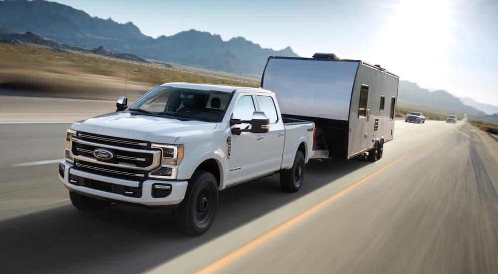 A white 2021 Ford F-250 is towing a camper on a highway.