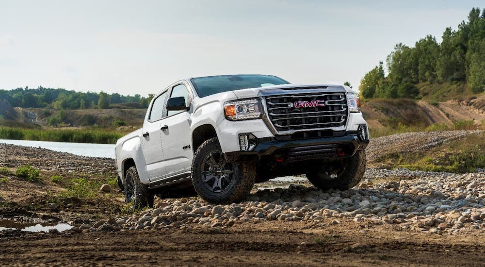 A white 2021 GMC Canyon AT4 is climbing over rocks on a trail.