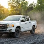 A white 2021 GMC Canyon AT4 is driving on a trail in the woods.