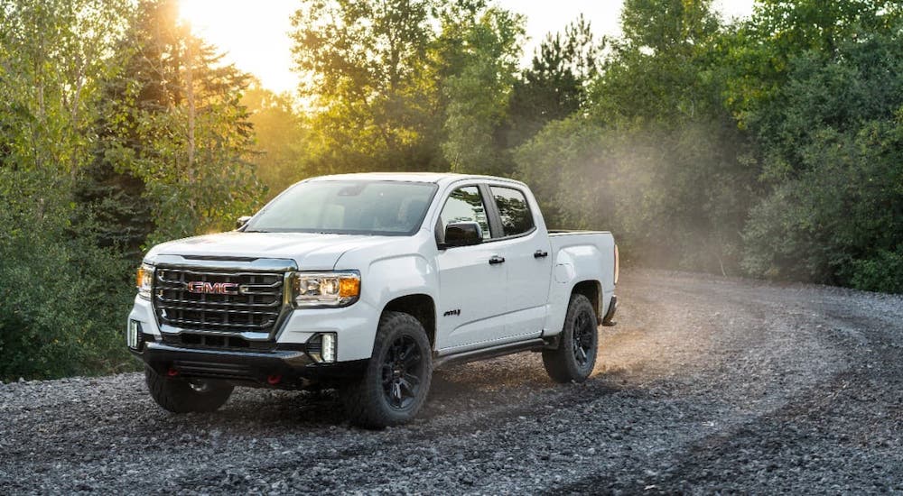 A white 2021 GMC Canyon AT4 is driving on a trail in the woods.