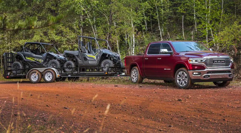 A red 2021 Ram 1500 is parked on dirt with a trailer filled with two UTVs.