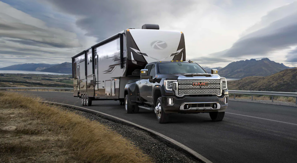 A black 2021 GMC Sierra 3500 is towing a camper down an open road with mountains in the back.