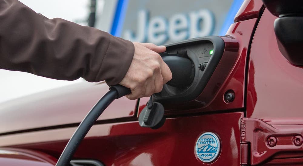 A closeup shows a hand plugging in a 2021 Jeep Wrangler 4xe.