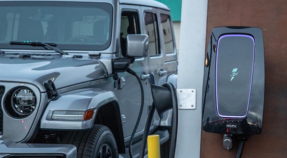A closeup shows the wall charger and a silver 2021 Jeep Wrangler 4xe that is charging.