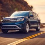 A dark blue 2021 Volkswagen Atlas is shown from the front, rounding a corner at sunset.