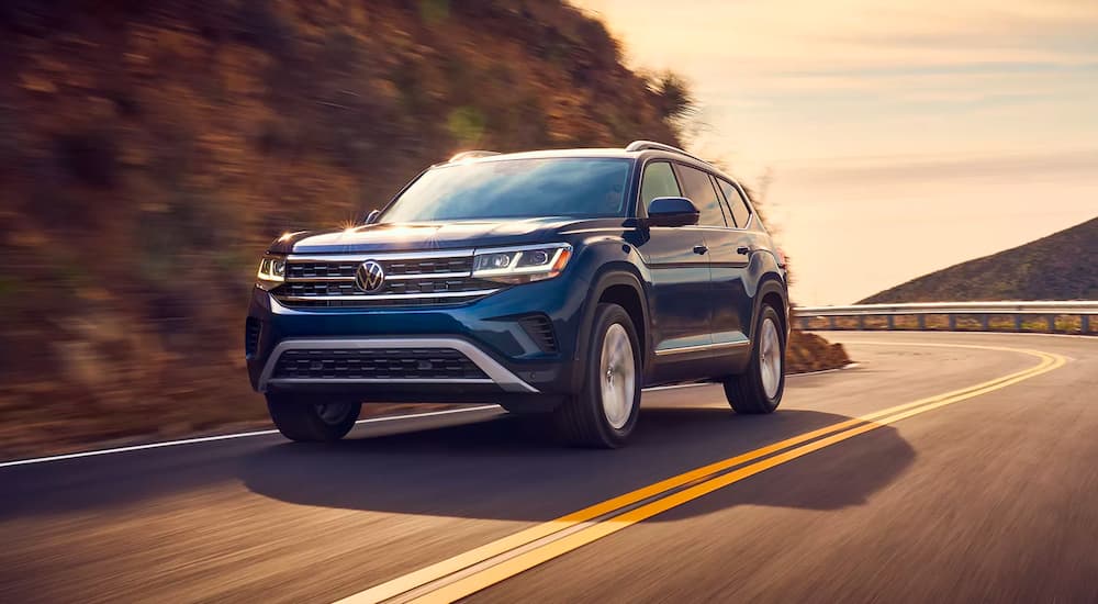 A dark blue 2021 Volkswagen Atlas is shown from the front, rounding a corner at sunset.