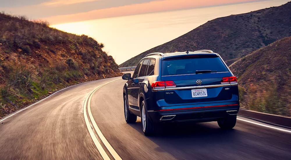 A dark blue 2021 Volkswagen Atlas is shown from the rear, rounding a corner at sunset.
