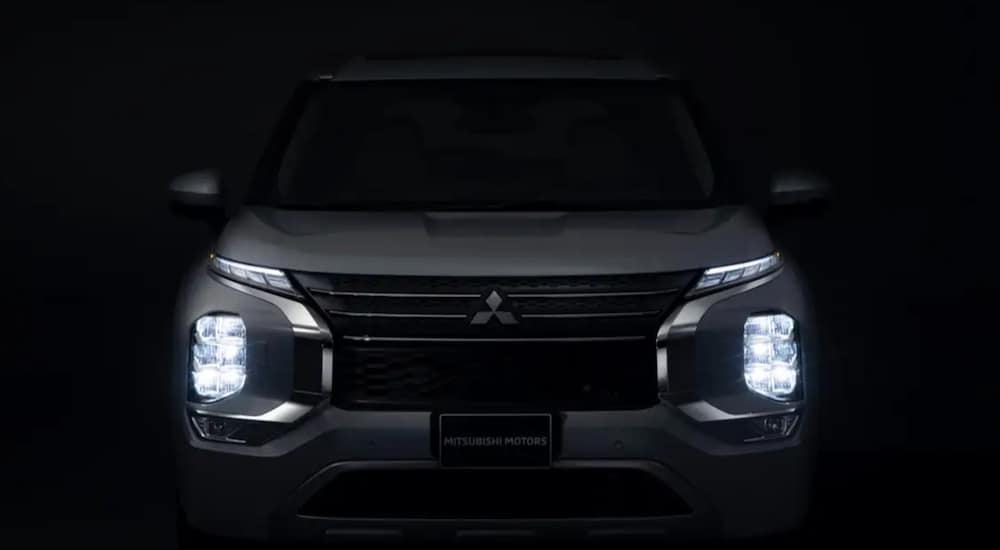 The front of a white 2022 Mitsubishi Outlander is shown with its parking lights on in the dark. 