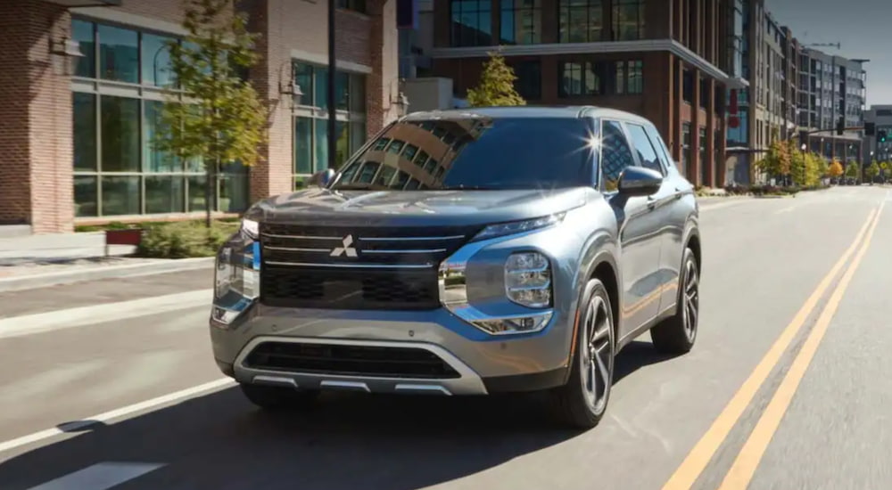 A silver 2022 Mitsubishi Outlander is driving on a two way road through an urban area.