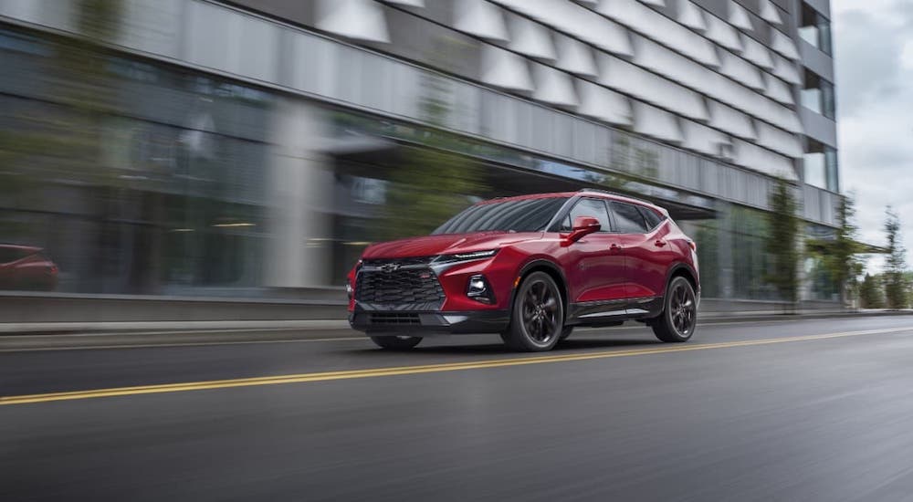 A red 2021 Chevy Blazer is driving in front of a modern building.