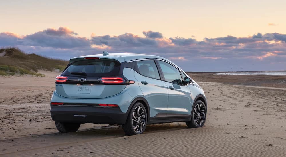 A light blue 2022 Chevy Bolt EV is parked on the beach at sunset.
