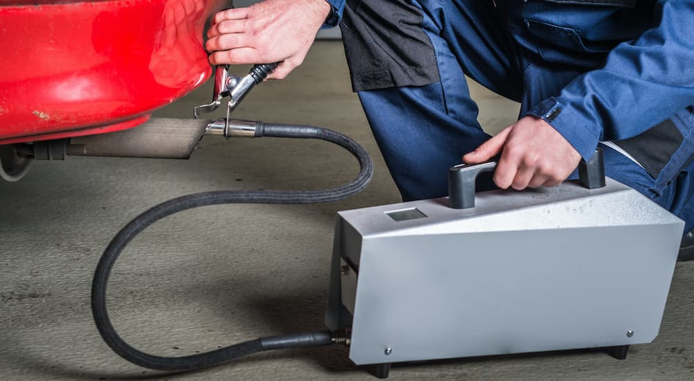 A mechanic is shown testing the emissions on a red car.