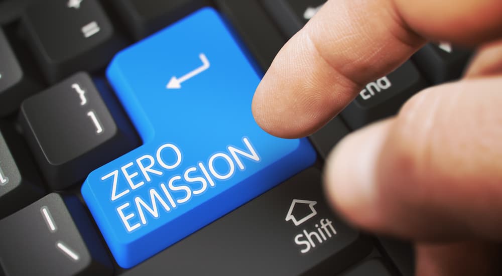 A finger is shown pressing a blue zero emissions return key on a keyboard.