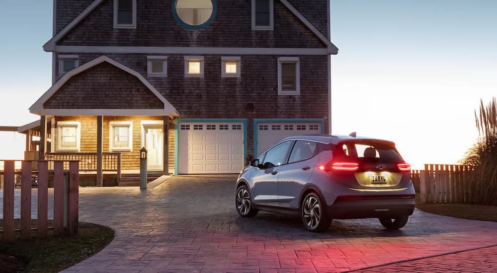A light blue 2022 Chevy Bolt EV is parked outside of a beach house at dusk.