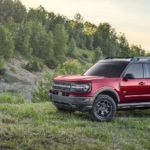 A red 2021 Ford Bronco Sport from a local Ford Bronco Sport dealer is parked in front of a hill covered in trees.