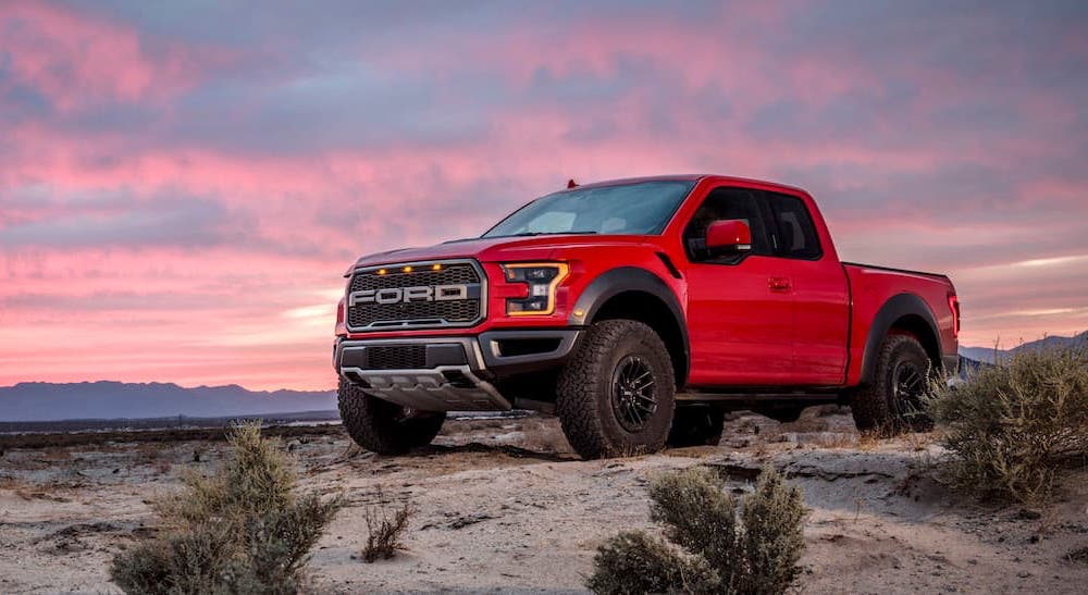 A red 2021 Ford F-150 Raptor is shown from the side parked with a sunset in the background.