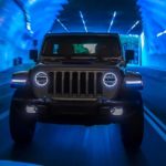 A silver 2021 Jeep Wrangler 4xe is shown from the front driving in a blue tunnel after leaving a Jeep dealer.