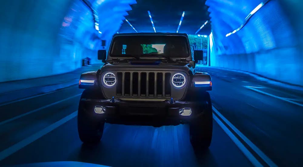 A silver 2021 Jeep Wrangler 4xe is shown from the front driving in a blue tunnel after leaving a Jeep dealer.
