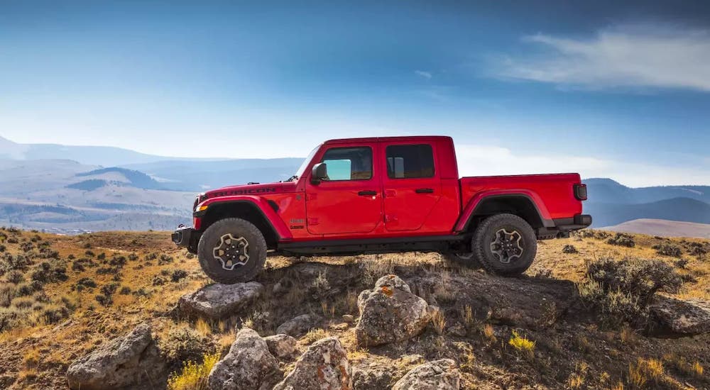 A great option for a Jeep lease, a red 2021 Jeep Gladiator, is shown from the side driving over rocks.