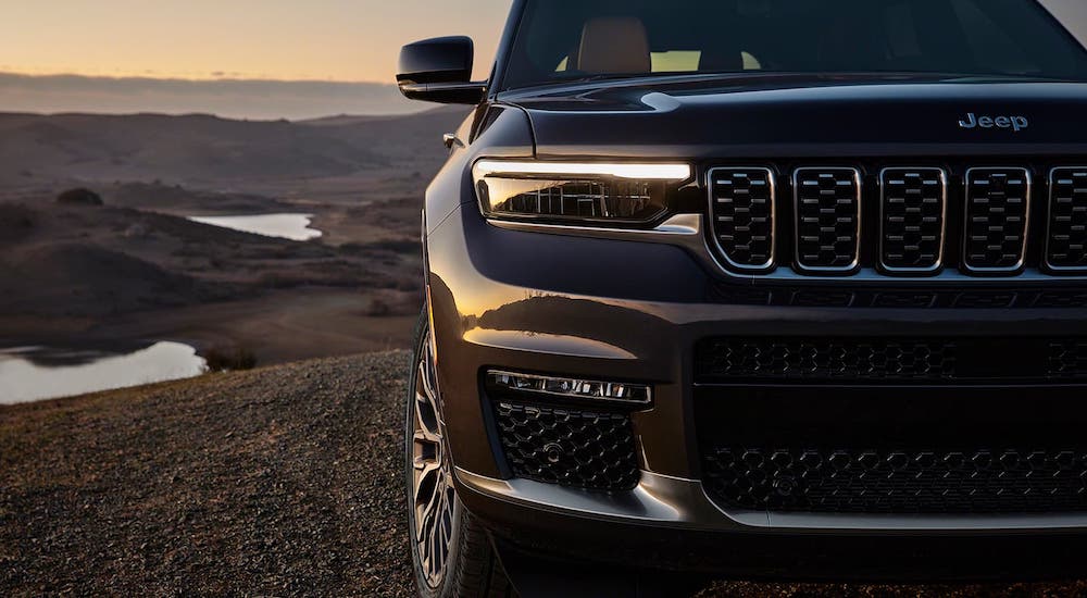 A closeup shows the passenger headlight and grille on a black 2021 Jeep Grand Cherokee L in front of a valley.