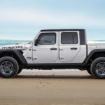 A white 2021 Jeep Gladiator is shown from the side parked on a beach next to a surfer.
