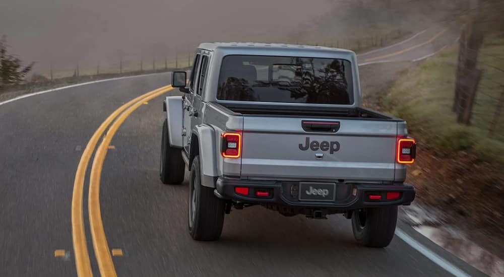 A grey 2021 Jeep Gladiator is shown from the back driving on a two way mountain road.