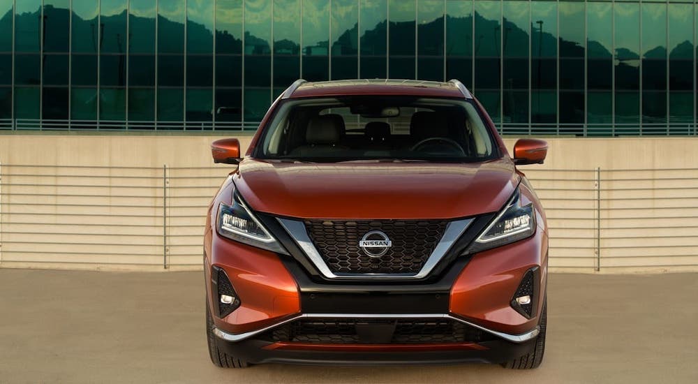 A dark orange 2021 Nissan Murano is shown from the front parked in front of a glass building.