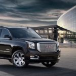 A black 2016 GMC Yukon Denali is parked outside of a modern glass building.