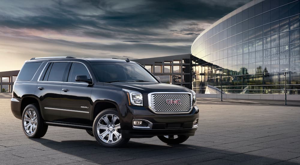 A black 2016 GMC Yukon Denali is parked outside of a modern glass building.