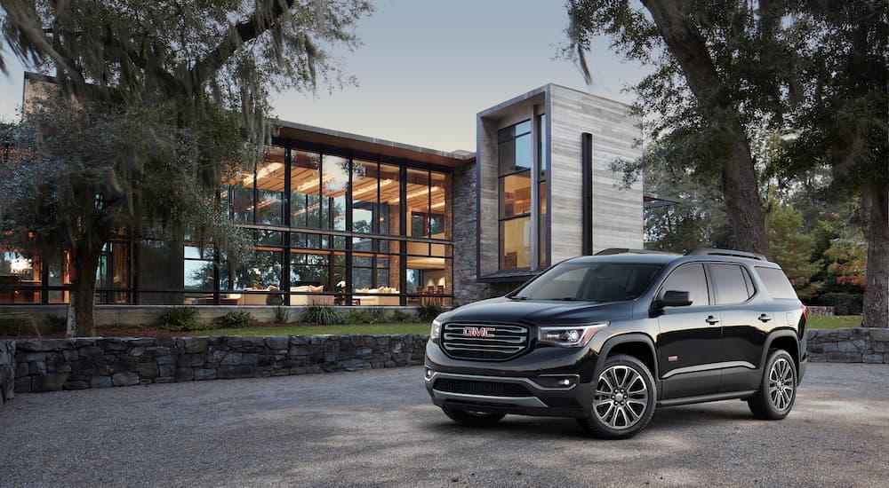 A black 2018 GMC Acadia All-Terrain is parked outside of a modern house.