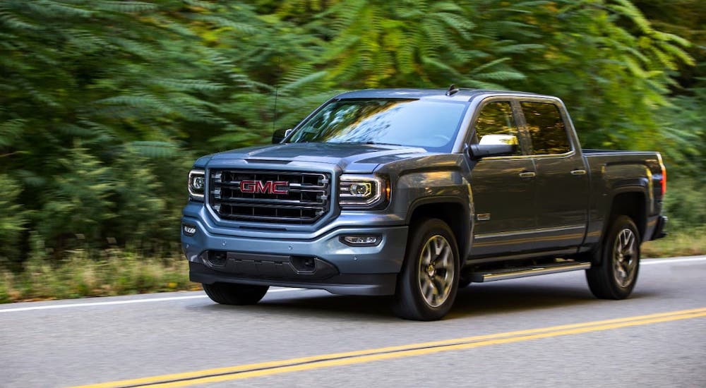 A slate blue 2017 GMC Sierra All Terrain is driving in front of trees.