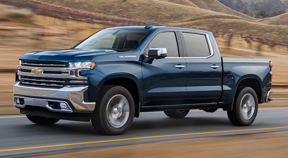 A blue 2021 Chevy certified pre-owned Silverado is shown from the side driving down an open road.