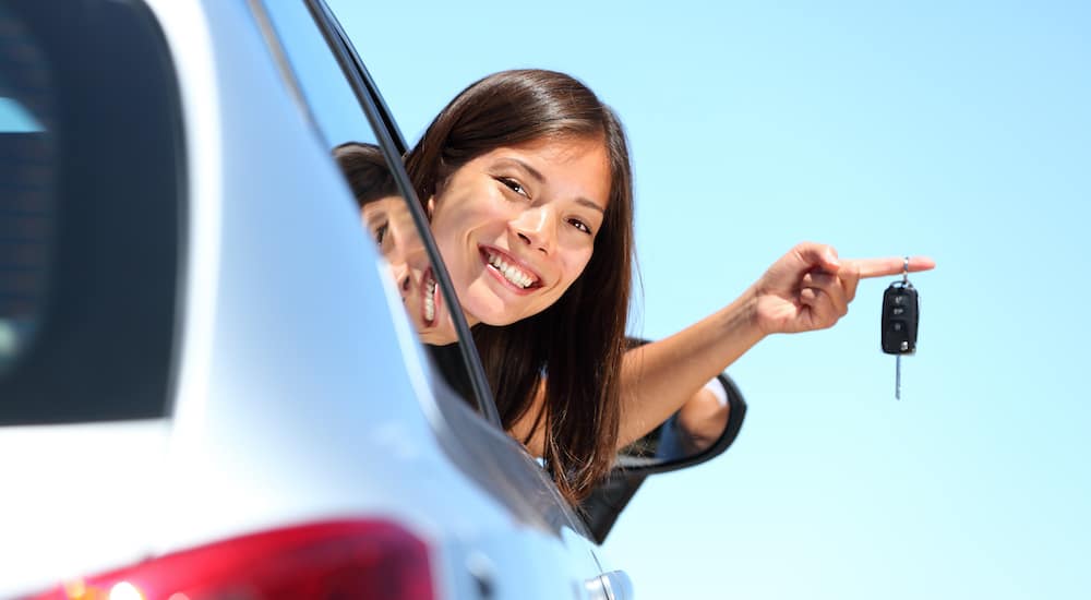 A teen driver is sticking her head out the window of a car while holding keys.