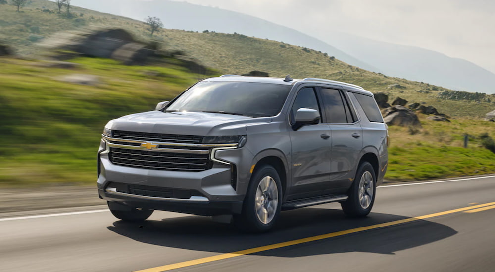 A silver 2021 Chevy Tahoe is driving down an open road under a blue sky.