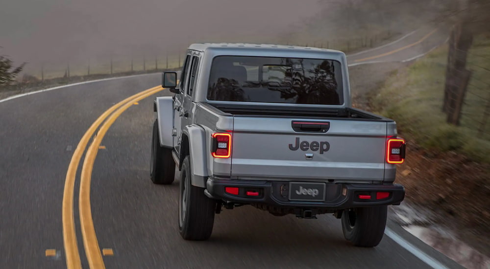 A silver 2021 Jeep Gladiator is shown from the rear as it drives down a winding road.