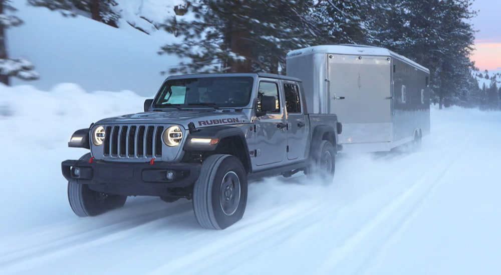 A 2021 silver Jeep Gladiator is towing a closed trailer through snow.
