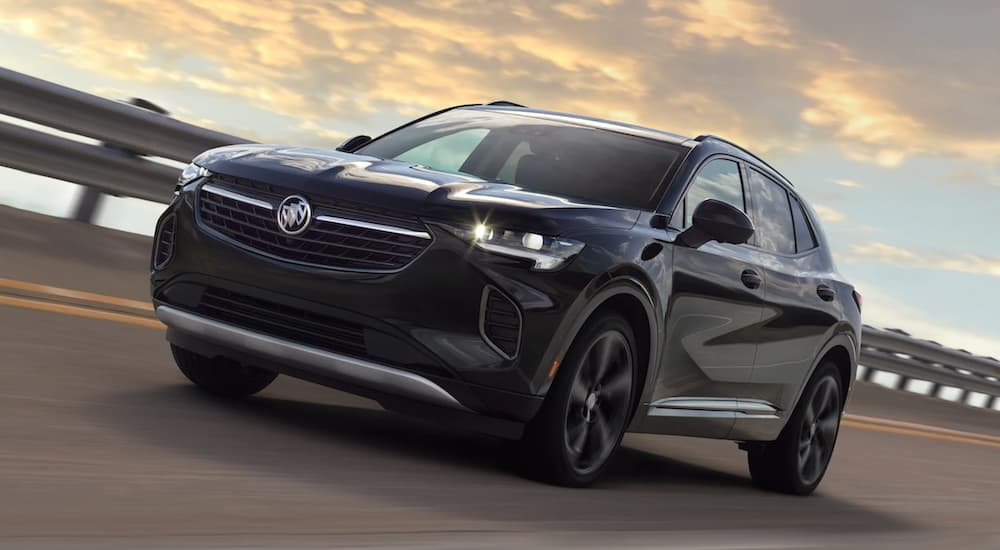 A black 2021 Buick Envision is driving over a bridge at sunset.