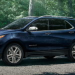 A blue 2021 Chevy Equinox is shown from the side parked in a driveway surrounded by forest after winning a 2021 Chevy Equinox vs 2021 Honda CR-V comparison.