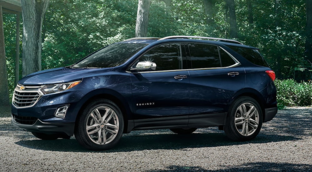 A blue 2021 Chevy Equinox is shown from the side parked in a driveway surrounded by forest after winning a 2021 Chevy Equinox vs 2021 Honda CR-V comparison.