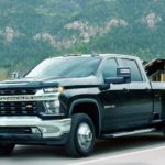 A black 2021 Chevy Silverado 3500HD is towing construction equipment.