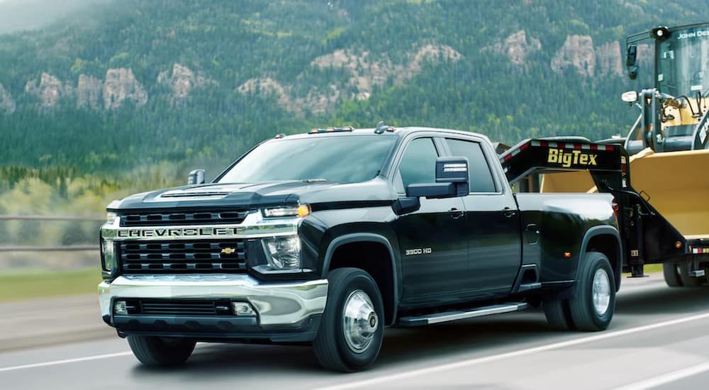 A black 2021 Chevy Silverado 3500HD is towing construction equipment.