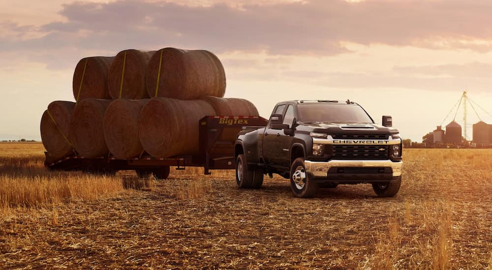 A black Chevy Silverado 3500HD is parked in a field towing hay.