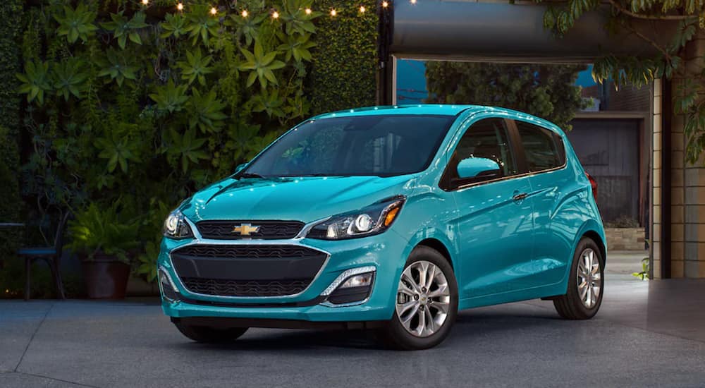 A turquoise 2021 Chevy Spark is parked outside of a modern house.