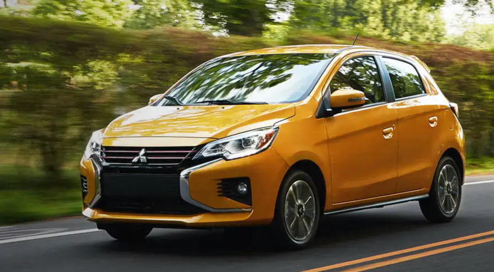 A yellow 2021 Mitsubishi Mirage is shown from the side driving down a two way road. 