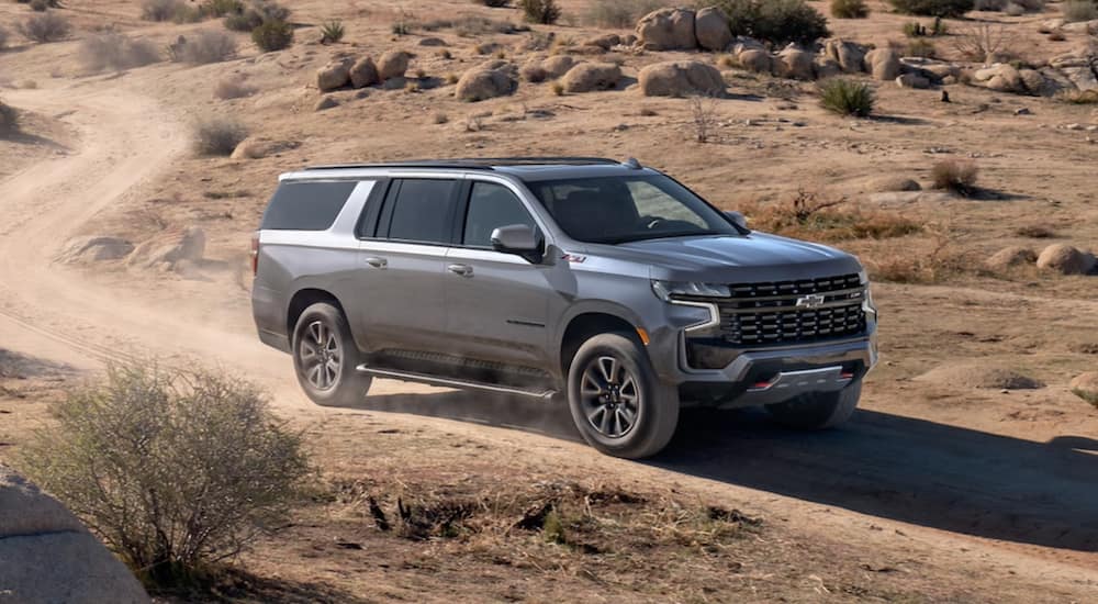 A grey 2021 Chevy Suburban is driving down a dirt road in a desert.