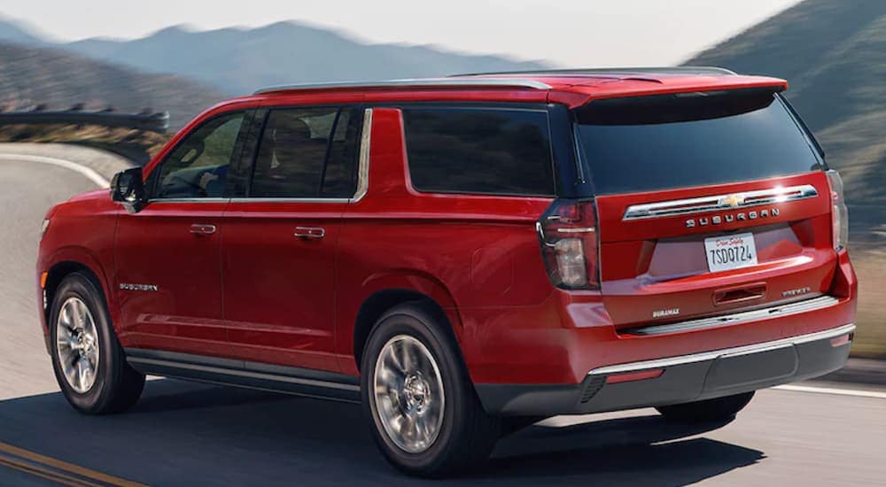 A red 2021 Chevy Suburban is shown from the back driving down an open road in front of a mountain.