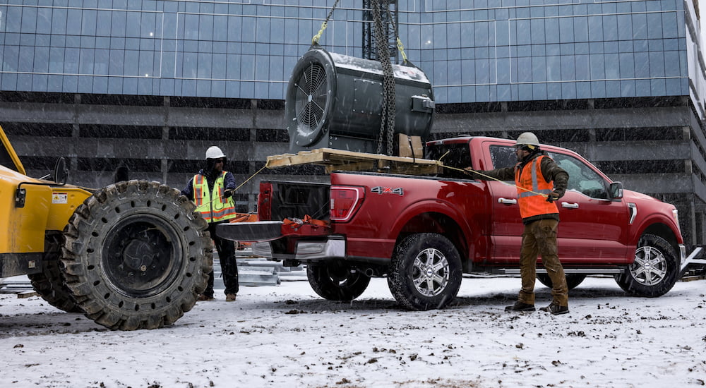 A red 2021 Ford F-150 is being used to carry heavy construction materials in front of a construction site.