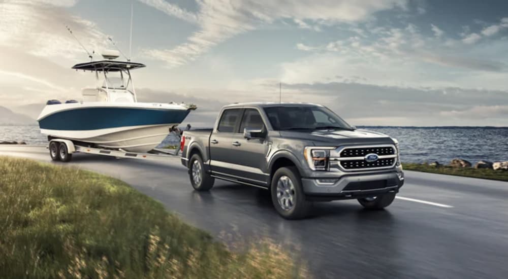 A silver 2021 Ford F-150 is towing a boat on a road next to the ocean.