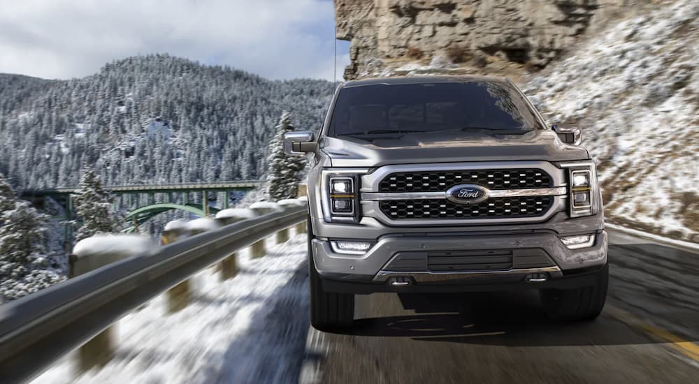 A grey 2021 Ford F-150 is shown from the front driving on a snowy road.