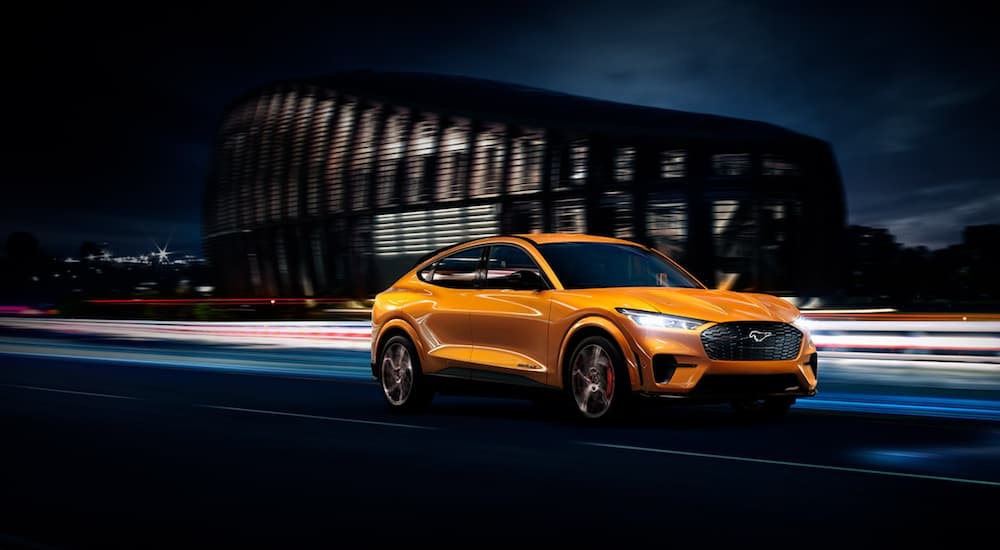 An orange 2021 Ford Mustang Mach-E is driving at night through a city.